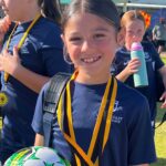 South Coast Baptist College student Mia smiling while holding a football and wearing her MVP medal